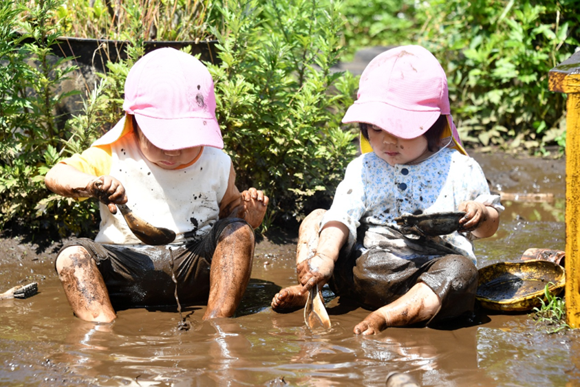 Hai em bé mầm non tại Trường Mầm non Kuraki Nagata trong giờ hoạt động ngoài trời, đang chơi với nước